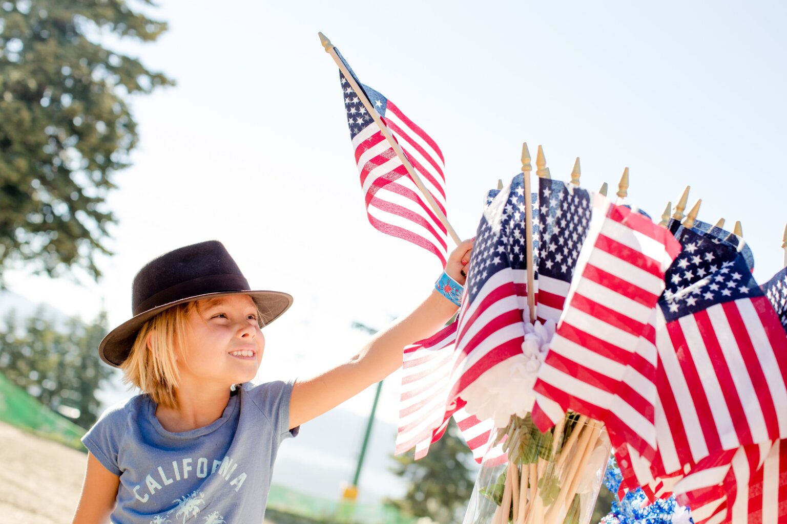 A boy in a California T-shirt picking up a small American flag from a vase of other little American flags for the Fourth of July.
