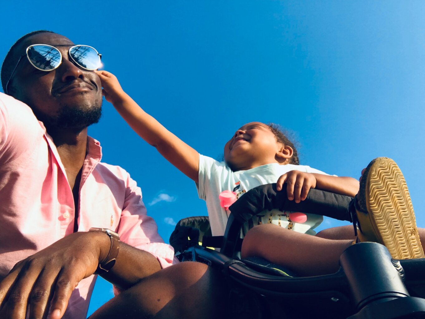 A baby playing with the sunglasses on their Dad's face.