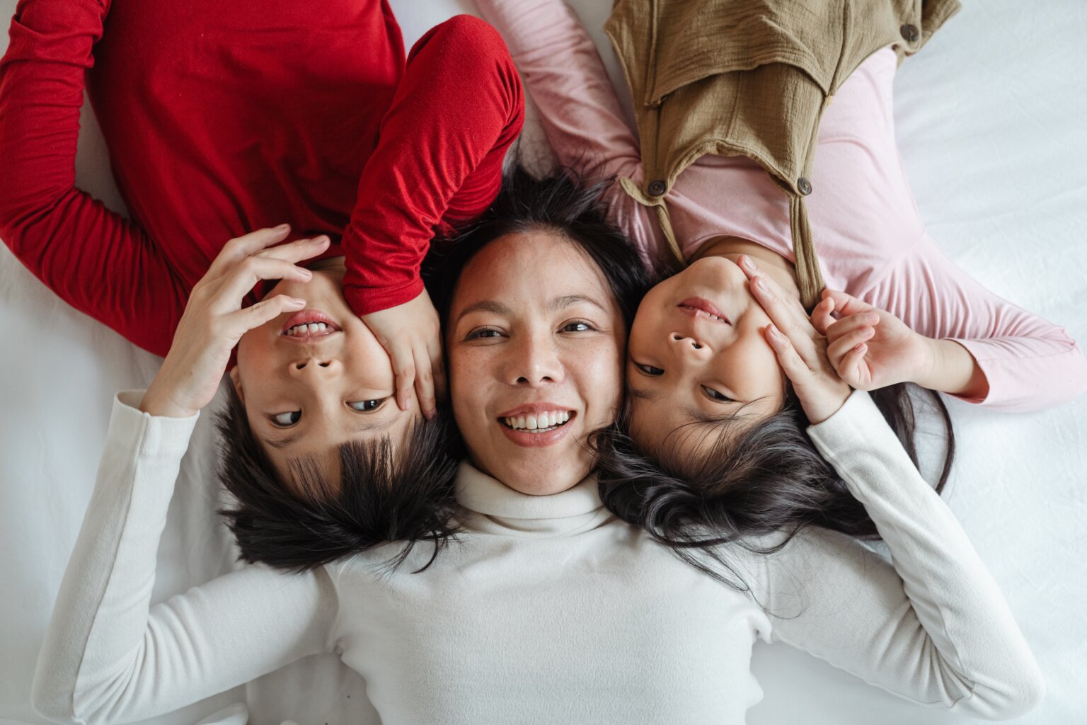 A mom and her son and daughter lying on a bed together smiling.