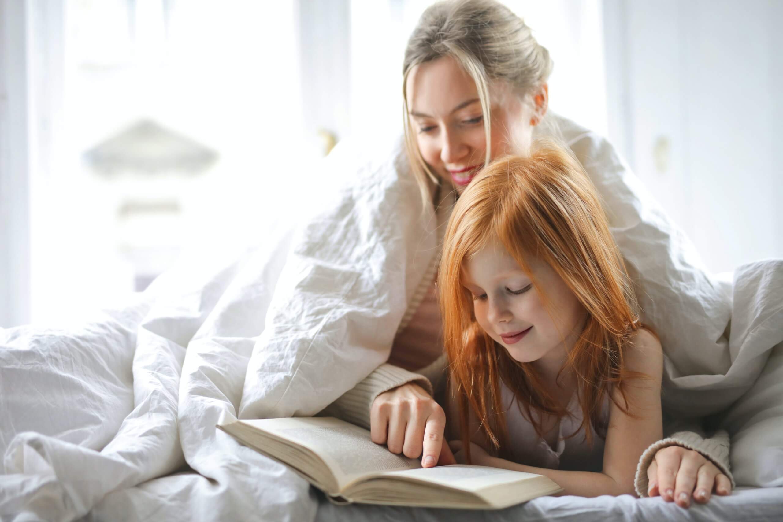 Mother and daughter reading a book together on a bed.