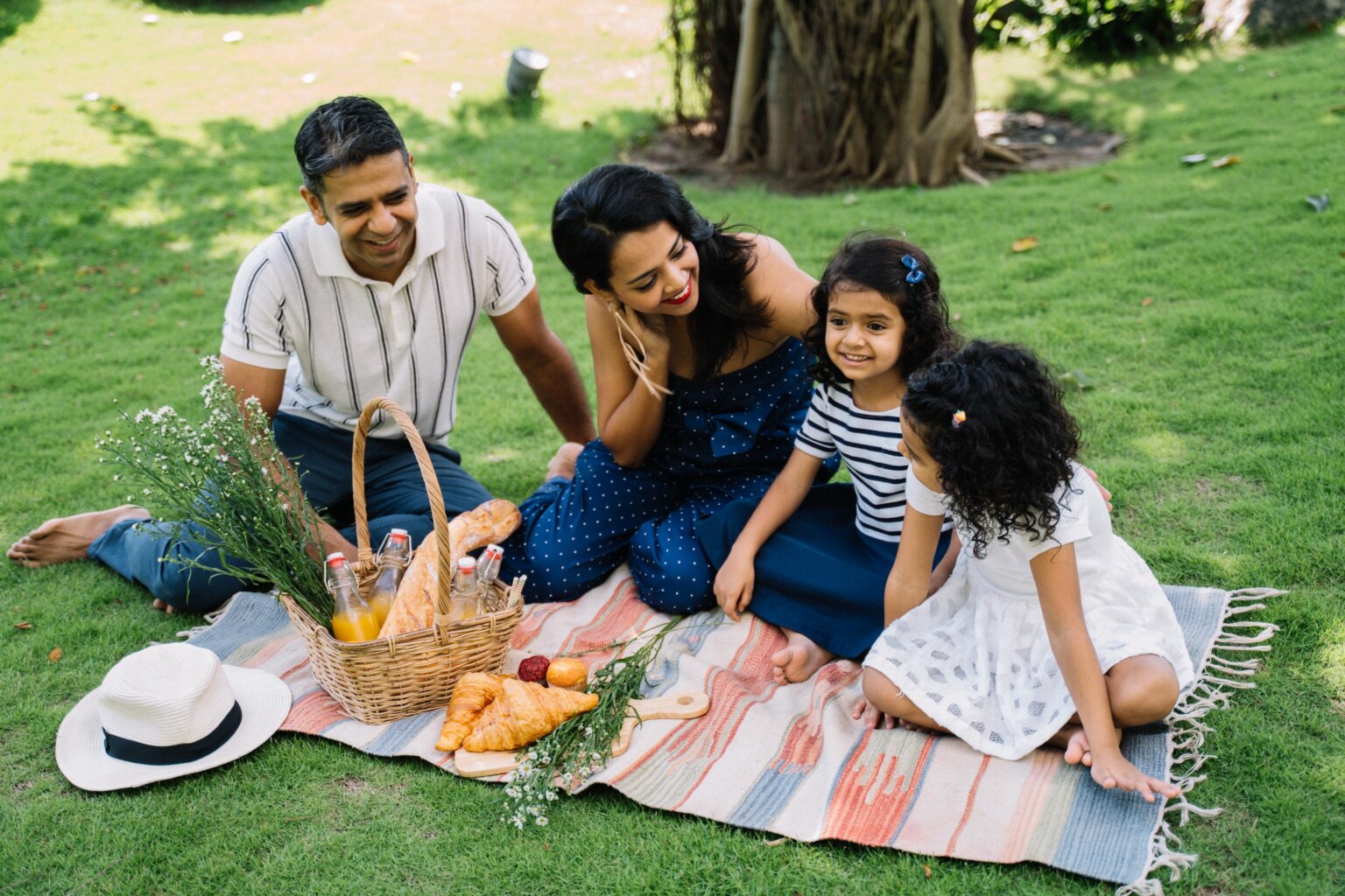 A dad, mom, and their two daughters having a picnic on the grass.
