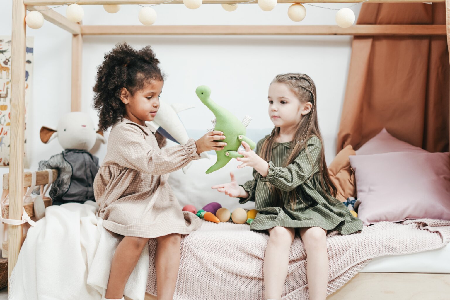 Two young girls holding a stuffed toy dinosaur between them.