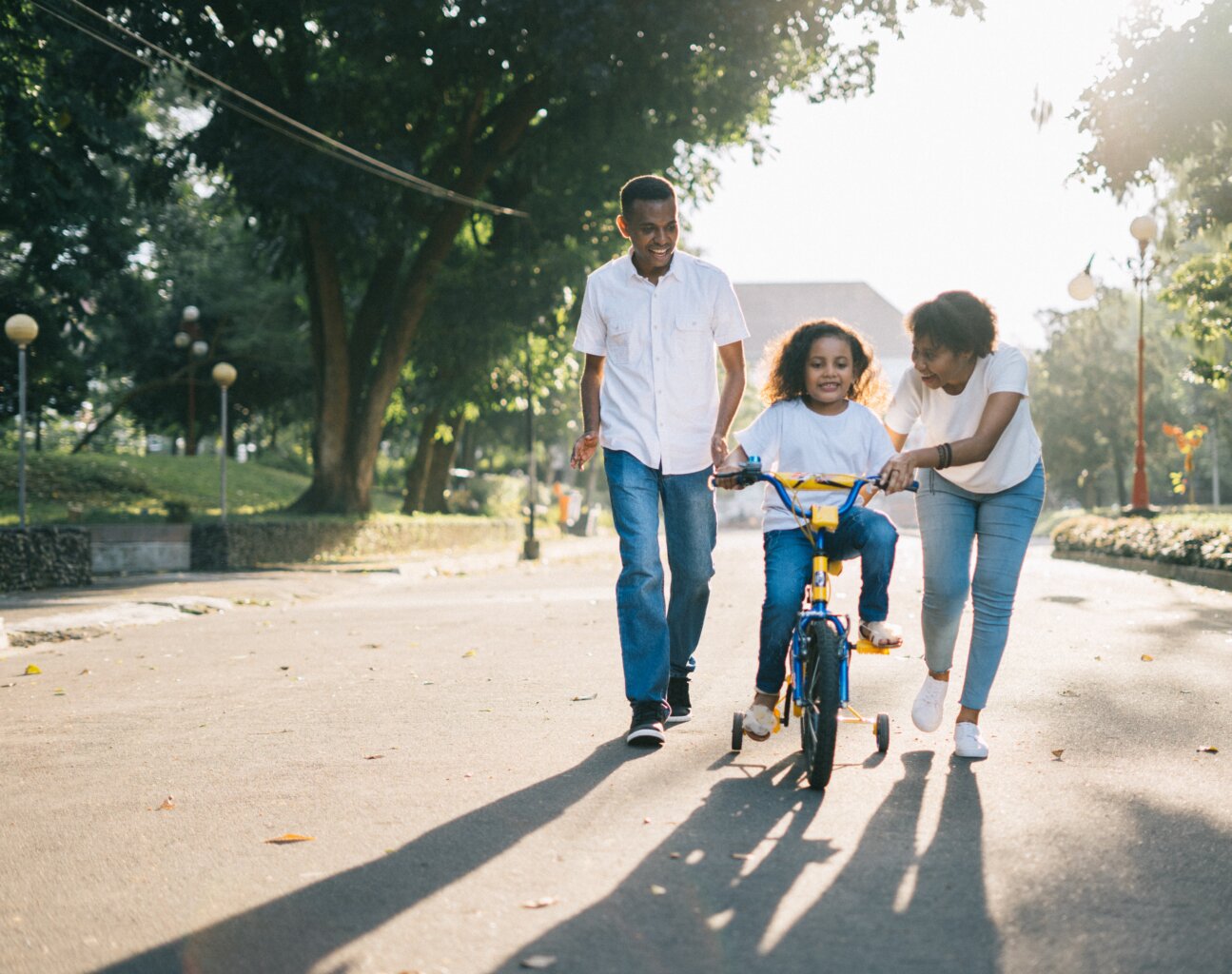 Parents, a mother and father, helping their daughter ride a bike for the first time.