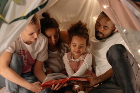 A mom and dad reading with their two daughters in a blanket fort.