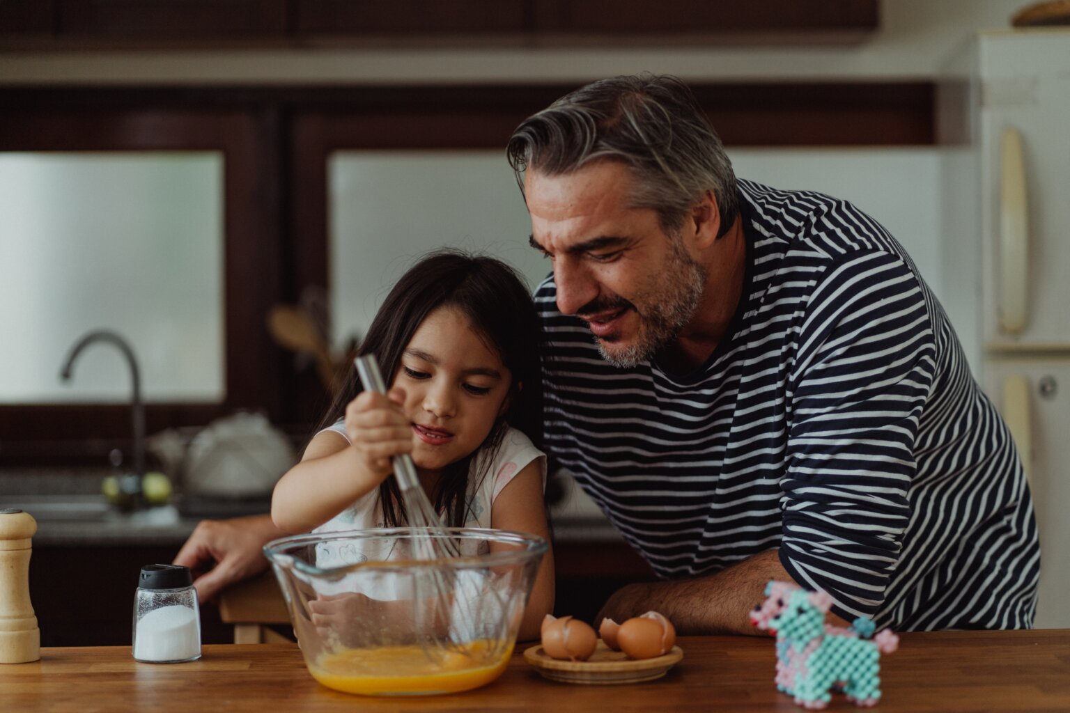 A dad helping his daughter whisk eggs.
