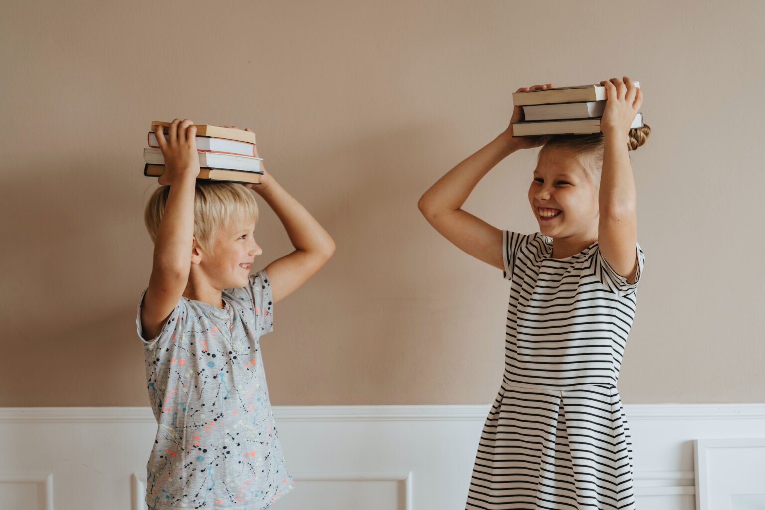 A brother and sister with a stack of books on their heads.