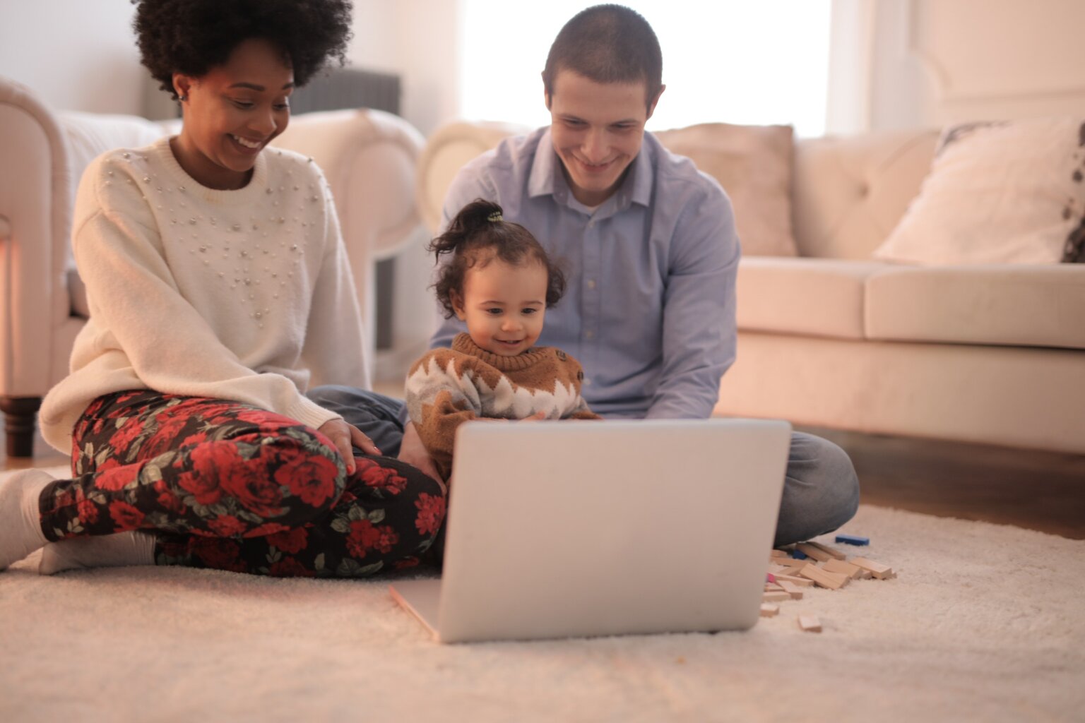 A dad, mom, and daughter laughing at a video on a computer while sitting on the floor.
