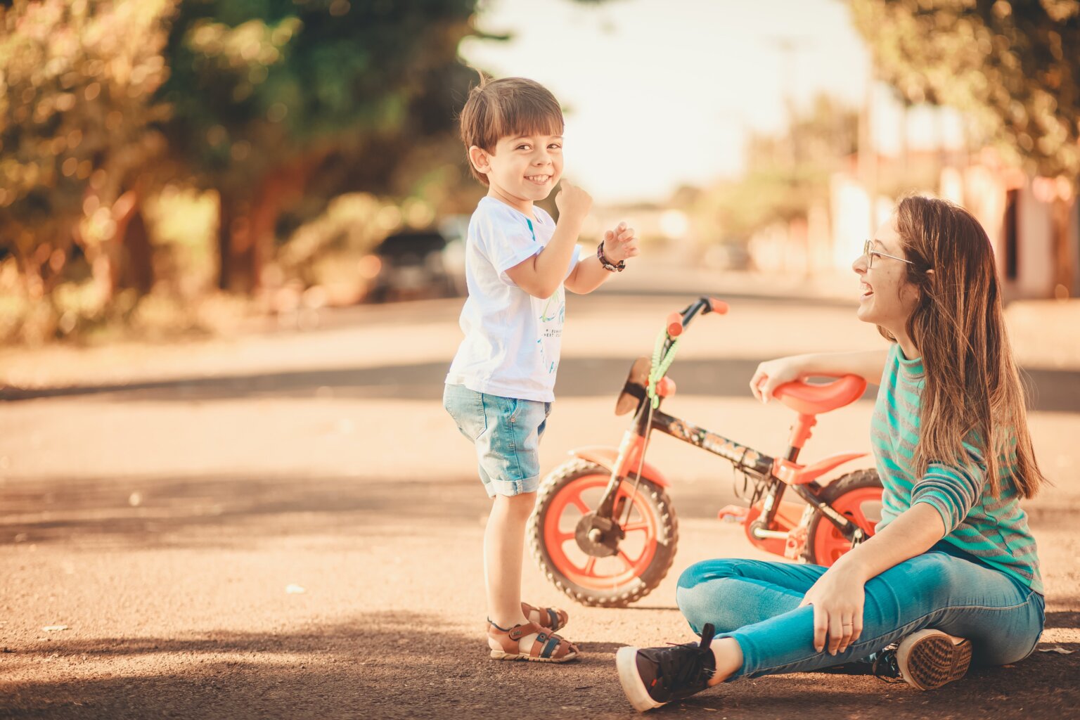 A mom and her son smiling while sitting on the ground with a bike.
