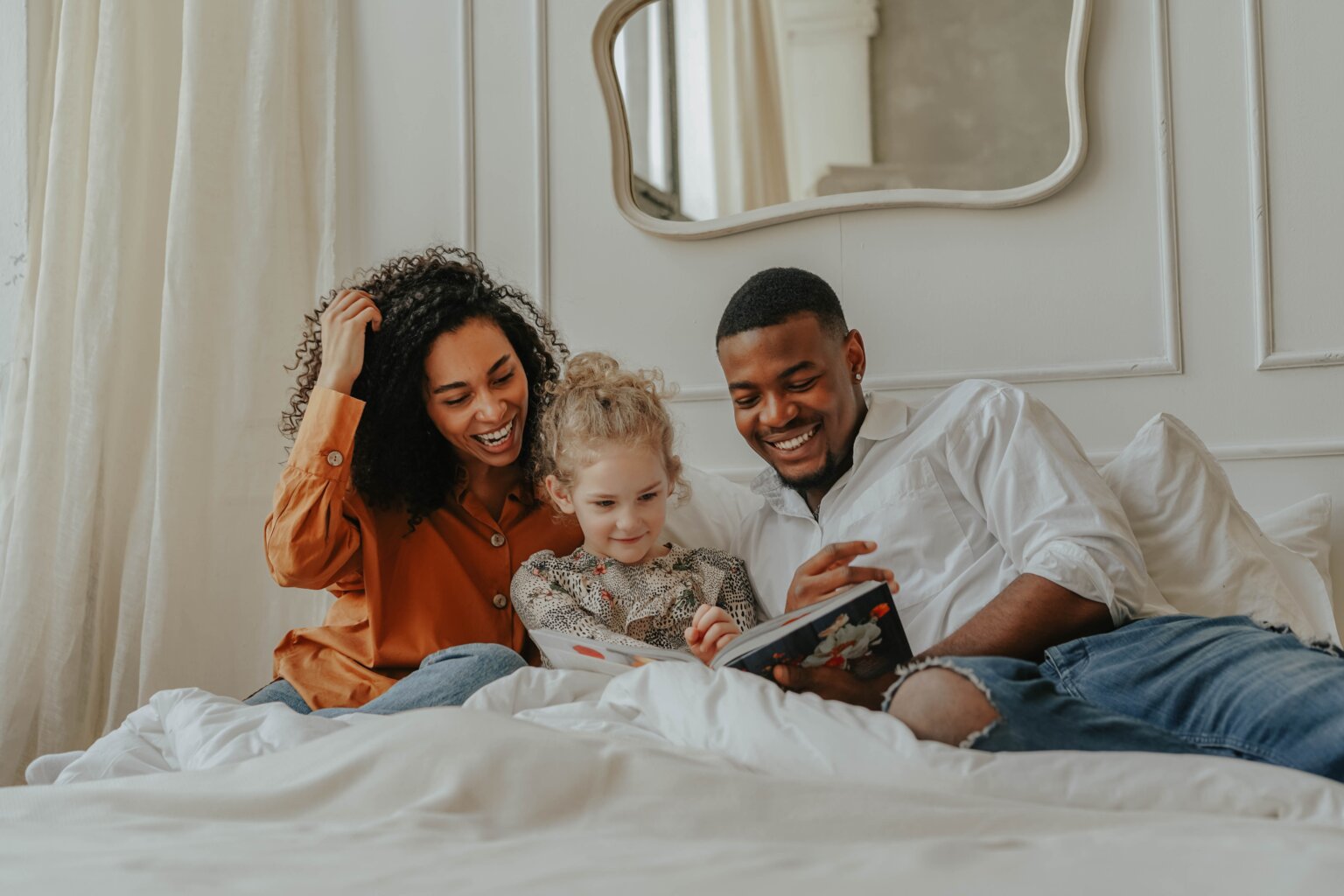 A mom and dad reading with their daughter on their bed.