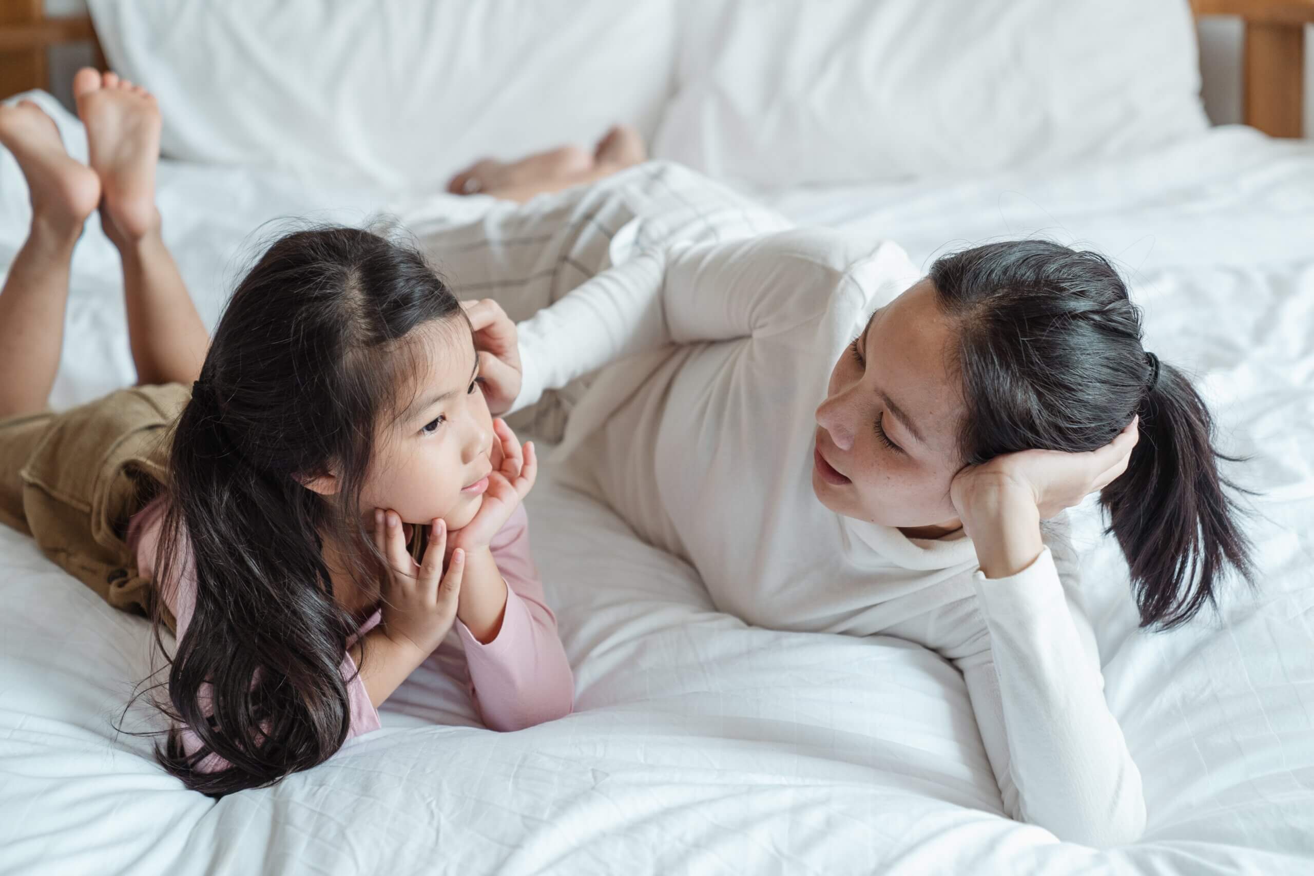 A mom and daughter talking on a bed.