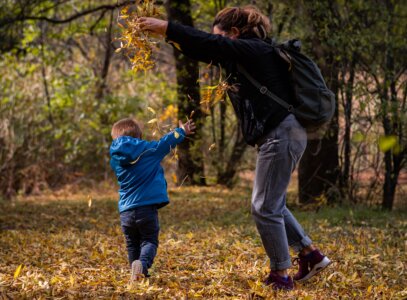 A parent and child playing in fallen leaves during the fall season.