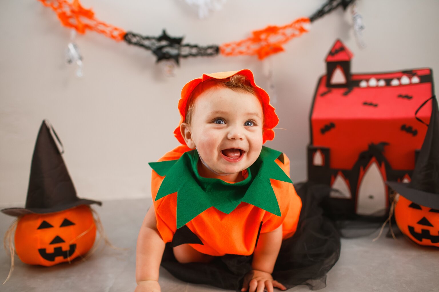 Smiling baby dressed in a pumpkin Halloween costume.