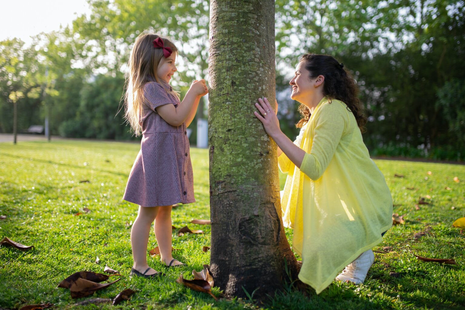 A mom and daughter playing around a tree.