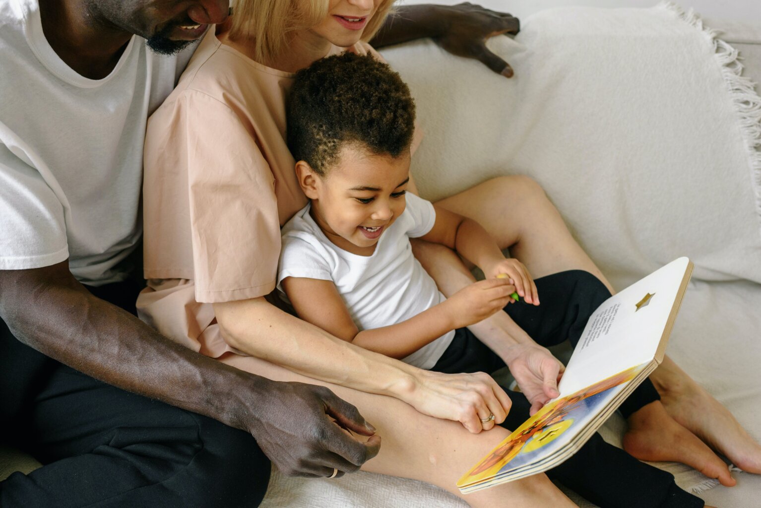 A father, mother, and toddler reading a board book together to improve reading skills.