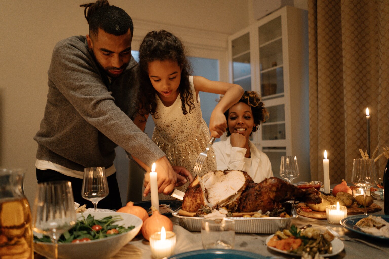 A dad helping his daughter carve a turkey at Thanksgiving dinner while the mom watches.