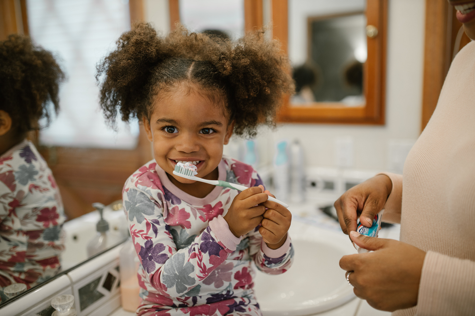 A girl practicing healthy habits by brushing her teeth with her mom.