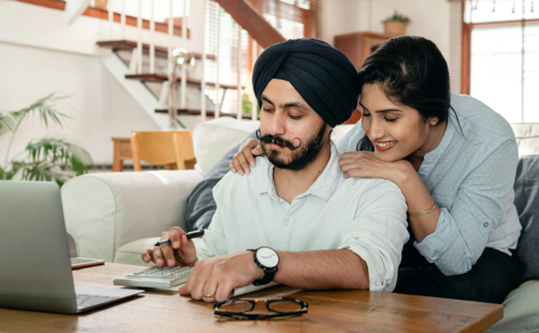 A cheerful couple working on the family finances while sitting at the coffee table with a calculator.