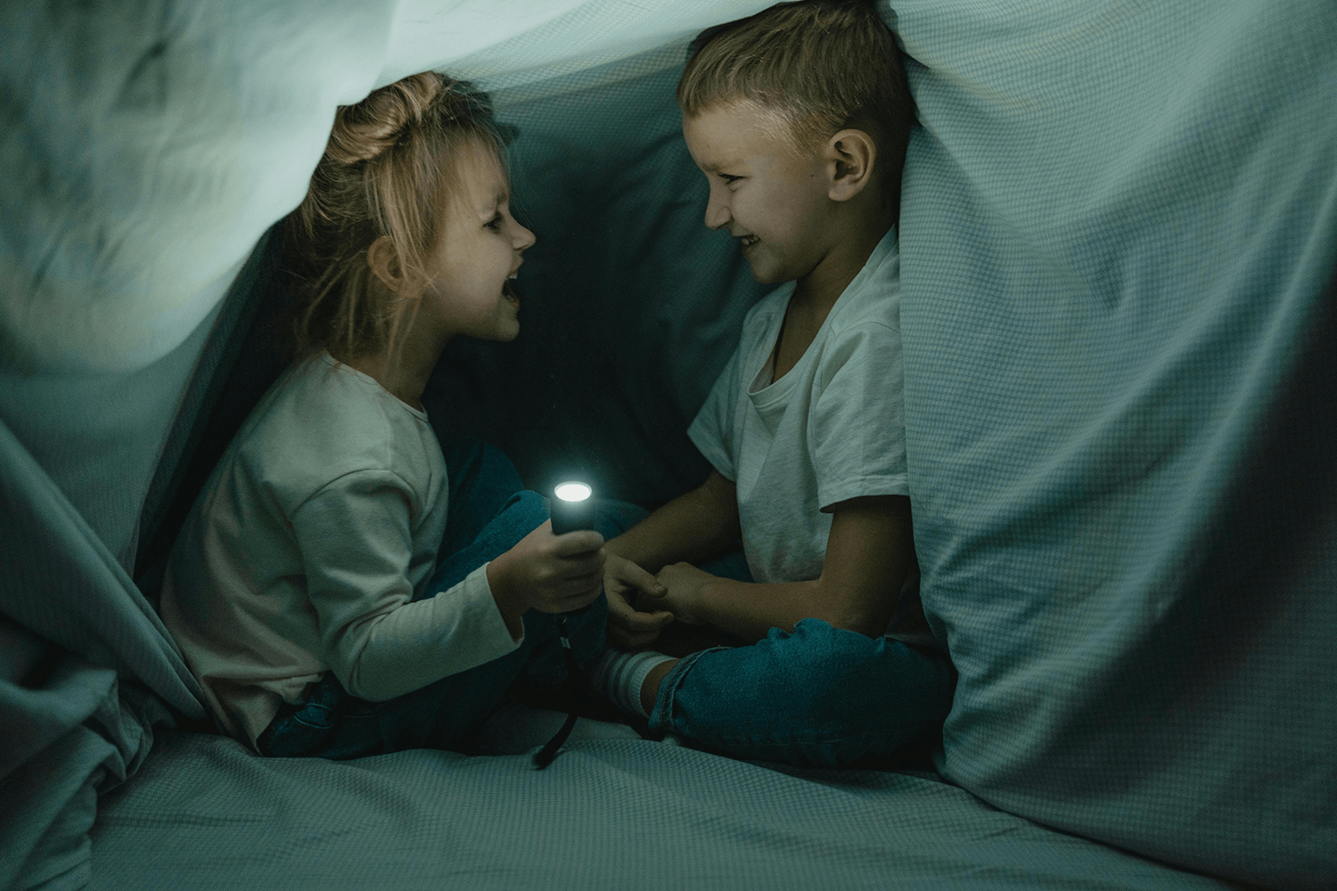 A boy and girl telling stories to each other in a blanket fort at story time.