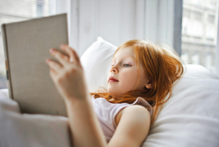 A girl reading a book while lying on a bed.