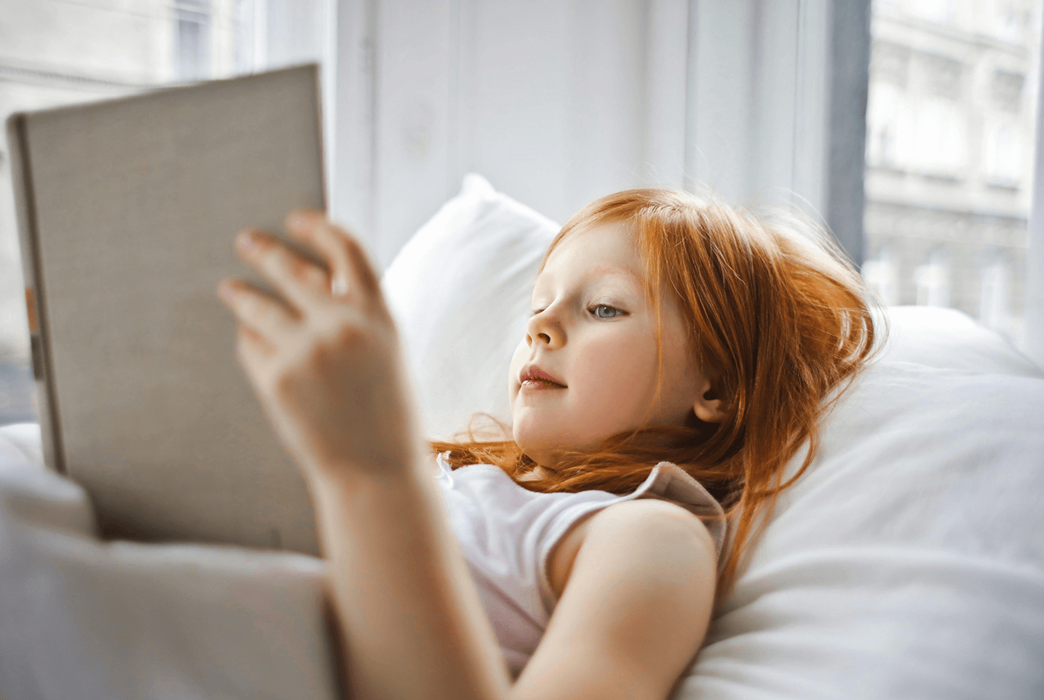 A girl reading a book while lying on a bed.
