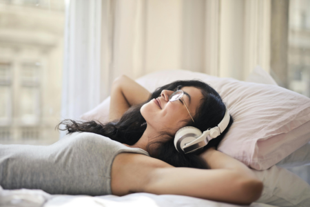 A woman lying on a bed while listening to music to take a break.